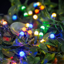 Close-up of multi-coloured globe LED string lights woven through green foliage, creating a vibrant festive display for Christmas trees, garden decorations and seasonal indoor or outdoor lighting.
