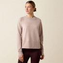 Front view of a model wearing a light blush Ariat crewneck sweatshirt with a relaxed fit, tonal embroidered Ariat logo, ribbed crew neckline, cuffs, and hem.