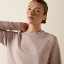 Close-up of the light blush Ariat crewneck sweatshirt featuring a tonal embroidered Ariat logo across the chest, a ribbed crew neckline, and raglan sleeves.