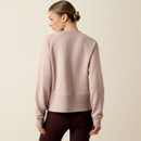 Back view of a model wearing a light blush Ariat crewneck sweatshirt with raglan sleeves, ribbed cuffs and hem, and a relaxed fit, paired with dark riding leggings.