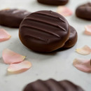 Close-up of Whitakers Rose Creams dark chocolates with smooth dark chocolate shells, styled with scattered rose petals to highlight the rose infused fondant centres.