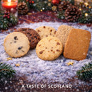 Assorted Scottish biscuits from Stewart's Scotland Tasty Biscuits selection displayed on a festive snow-effect surface with pine cones, fir branches and candlelight.