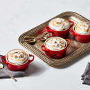 Four Le Creuset Cerise stoneware mini round casserole dishes filled with baked desserts topped with toasted meringue, arranged on a serving tray.