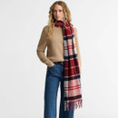 Model wearing a red, navy and cream tartan scarf with fringed edges, styled with a camel jumper and blue jeans.