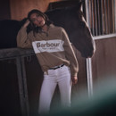 Woman wearing the Barbour women's beige quarter zip sweatshirt in a stable alongside a horse, showcasing the relaxed fit and embroidered logo design.