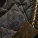 Close-up of the Barbour Icons Spey olive wax jacket highlighting quilted panels, tartan sleeve fabric, corduroy trim and brass zip.