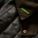 Close-up of the Barbour Icons Spey women's wax jacket showing the green Barbour pin badge, corduroy collar and quilted fabric.