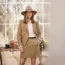 Woman wearing a Barbour beige felt fedora hat with a braided leather band and wide brim indoors with a tailored tweed outfit.