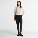 Full-length view of the Barbour women's cream cable knit roll neck jumper styled with dark jeans and knee-high leather boots.
