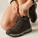 Close-up of a person tightening the laces on a brown waterproof hiking boot with padded ankle collar, metal speed hooks and durable outdoor construction.