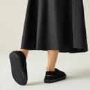 Rear view of black adjustable slingback mule slippers worn with a black midi skirt, highlighting the secure heel strap and textured outsole.