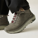 Close-up of a taupe waterproof hiking boot worn with outdoor trousers, highlighting the mid-cut ankle support and cushioned trail sole.