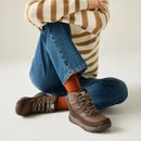 Women's brown waterproof hiking boots styled with blue jeans, striped knit jumper and rust-coloured socks for a casual outdoor-inspired look.