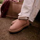 Close-up of tan faux suede waterproof ankle boots with plush faux fur trim, worn outdoors with cream trousers for warm winter comfort.