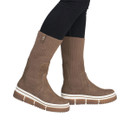 Model wearing Rieker women's tan slip-on boots with extended ribbed knit shaft and chunky platform soles.