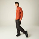 Child modelling a burnt orange half-zip fleece with black walking trousers and hiking shoes.