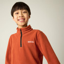 Close-up of child wearing a burnt orange half-zip fleece with embroidered Regatta Outdoors logo.