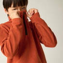 Child zipping up the high collar of a burnt orange half-zip fleece.