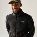 Man wearing a Regatta black and olive camouflage fleece jacket, sitting down and looking upwards with a green cap.
