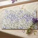 William Morris Willow Bough glass chopping board featuring the iconic leafy botanical design, displayed on a linen tablecloth beside a tied bundle of fresh lavender.