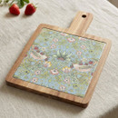 William Morris Strawberry Thief acacia serving board with a ceramic inlay featuring the iconic bird and floral design, displayed on a linen tablecloth with fresh strawberries.