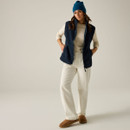Full-length view of a woman wearing the Regatta women's Navy Borg fleece gilet with cream trousers and a blue beanie.