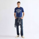 Male model wearing a blue Wrangler graphic T-shirt styled with dark blue denim jeans, a grey plaid shirt tied around the waist, and white sneakers for a casual everyday look.