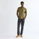 Male model wearing the Wrangler Olive Night graphic T-shirt with charcoal trousers and tan suede sneakers, creating a relaxed everyday outfit with understated heritage styling.