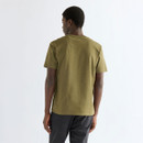 Male model wearing the Wrangler Olive Night graphic T-shirt with charcoal trousers and tan suede sneakers, creating a relaxed everyday outfit with understated heritage styling.
