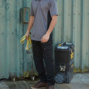 Black multi-pocket work trousers worn with a grey polo shirt and brown work boots in an industrial outdoor setting.
