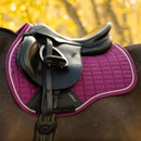 Close-up of a black English saddle on a purple LeMieux quilted saddle pad with silver piping, fitted to a dark horse.