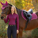 Rider standing beside a brown horse dressed in coordinated magenta LeMieux equestrian wear, fly hood and saddle pad.