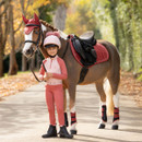 Young rider in pink equestrian clothing standing beside a horse wearing a red LeMieux saddle pad and matching accessories.