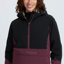 Close-up of the black and plum LeMieux jacket front, featuring a half zip, drawcord hood and branded front pocket flap.