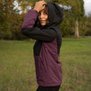 Side view of a woman wearing a black and plum LeMieux hooded jacket, showing the colour-block design and protective hood.