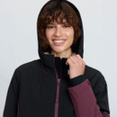 Close-up of a woman wearing the raised hood of a black and plum LeMieux jacket, showing the high collar and fleece lining.