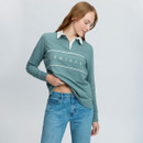 Woman wearing a sage green LeMieux long-sleeve polo shirt with white collar and branded chest panel, styled with blue jeans.