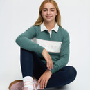 Seated studio view of a young rider wearing a green LeMieux polo top with white branded chest panel, navy riding leggings and pink trainers.