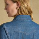 A woman with blonde hair wearing a denim western shirt, viewed from the side, showcasing gold earrings.