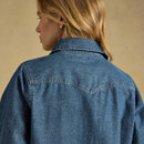 A woman wearing a blue denim shirt, showing the back view with a collar and western-style yoke design.