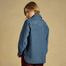 A person wearing a denim jacket facing away from the camera, set against a textured beige background.