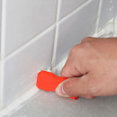 A hand using an orange caulking tool on white tiled surfaces, smoothing caulk.