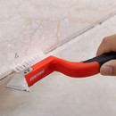 A hand holds a DEKTON CAULKING KIT tool with a metal blade and bristles, scraping along a tiled surface.
