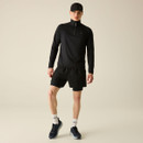 A model wearing a black long-sleeve zip top and black shorts, paired with socks and trainers.