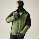 A man in an olive green and black jacket with gloves and a balaclava, looking upwards against a plain background.