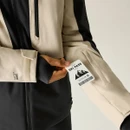 A person holds a ski pass next to the sleeve pocket of a beige and black Dare 2b Eagle IV jacket.