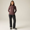 A woman stands wearing a long-sleeved, zip-up, maroon top and black trousers with a relaxed fit.