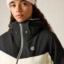 A woman wearing a black and cream hooded jacket with a logo on the chest, paired with a light pink beanie.