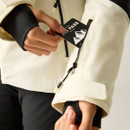 A person inserting a ski pass into a zippered pocket on a cream-coloured jacket sleeve.