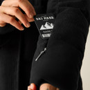 A person is pulling a ski pass from a zipped pocket of a black cord jacket.